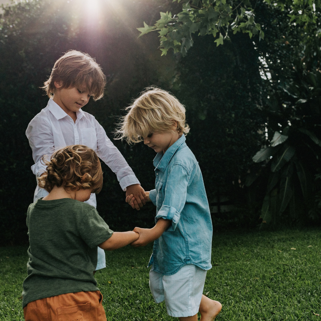 Three boys holding hands in a circle outdoors on the grass